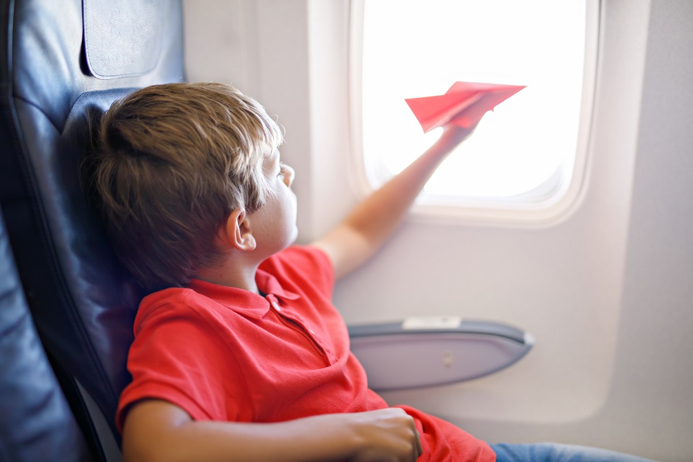 Little kid boy playing with red paper plane during flight